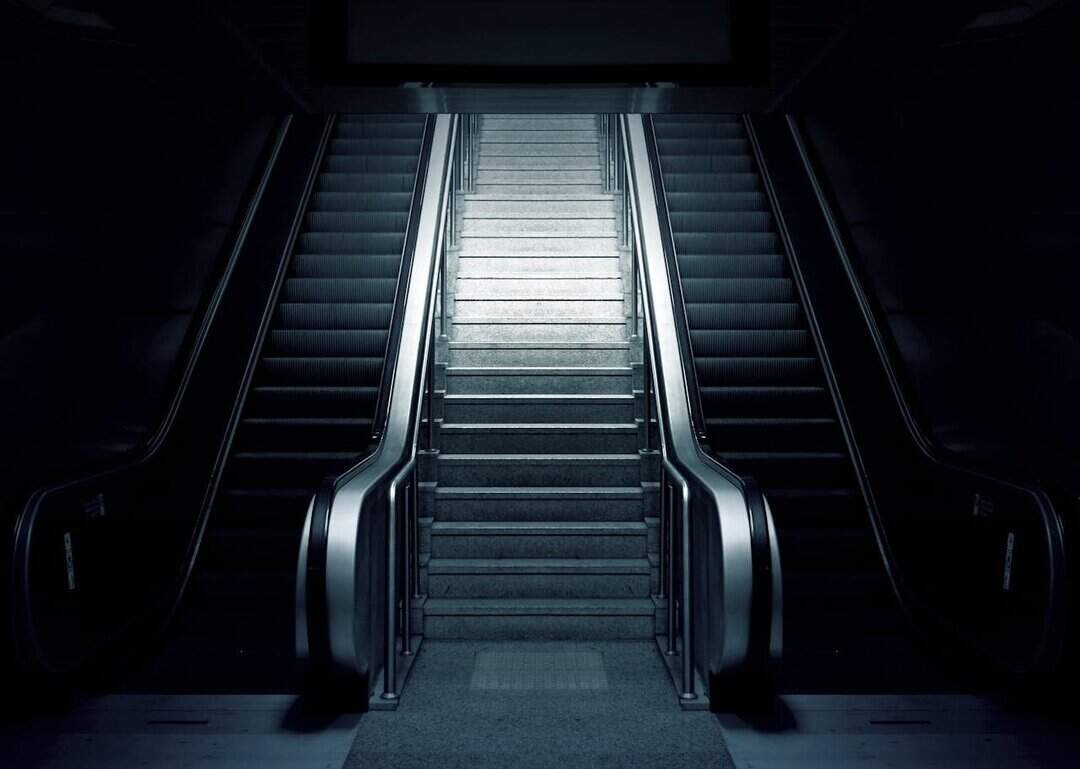 Dramatic contrast of dark escalators and illuminated stairs in an underground station.